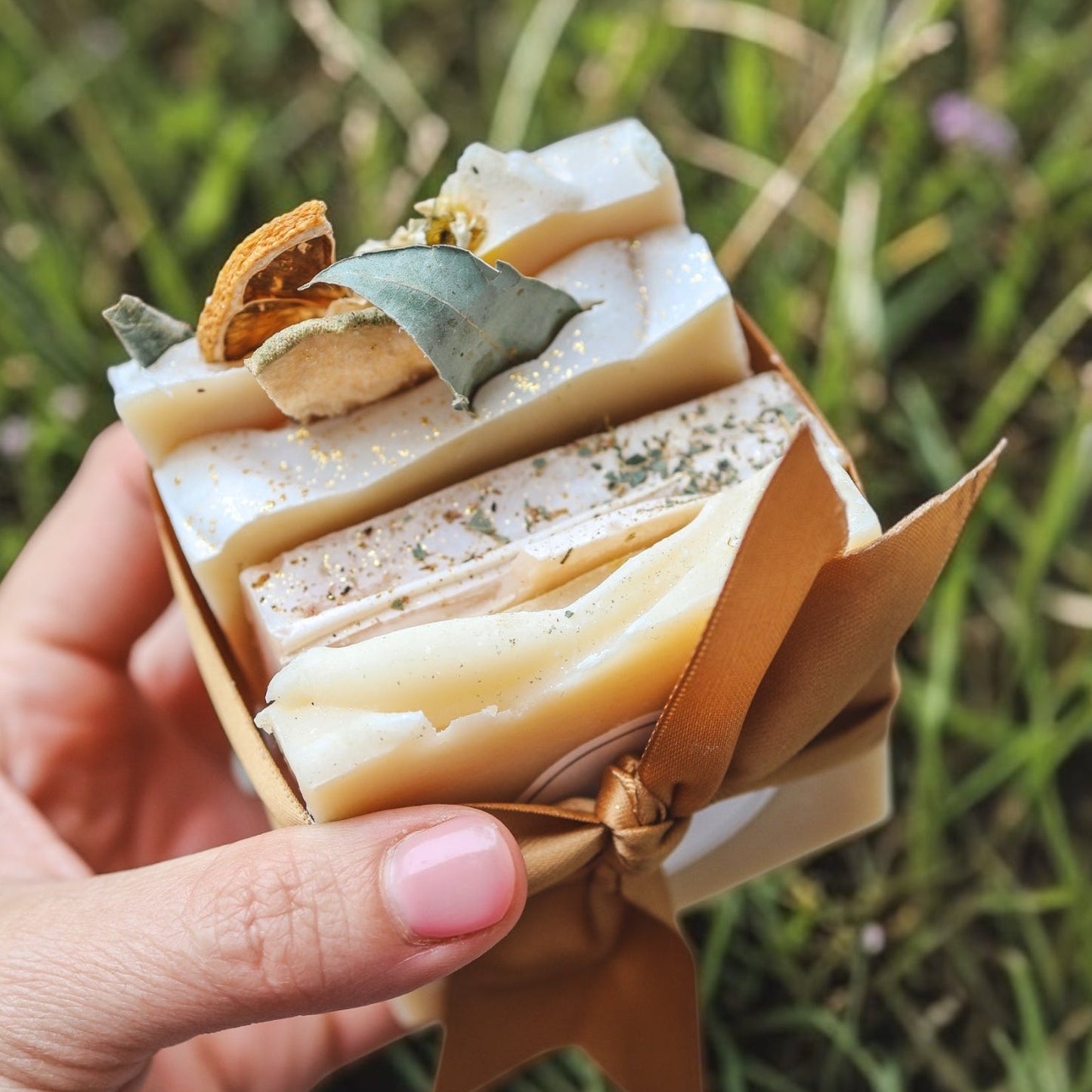Hand holding a small bundle of soap bars against a grassy background