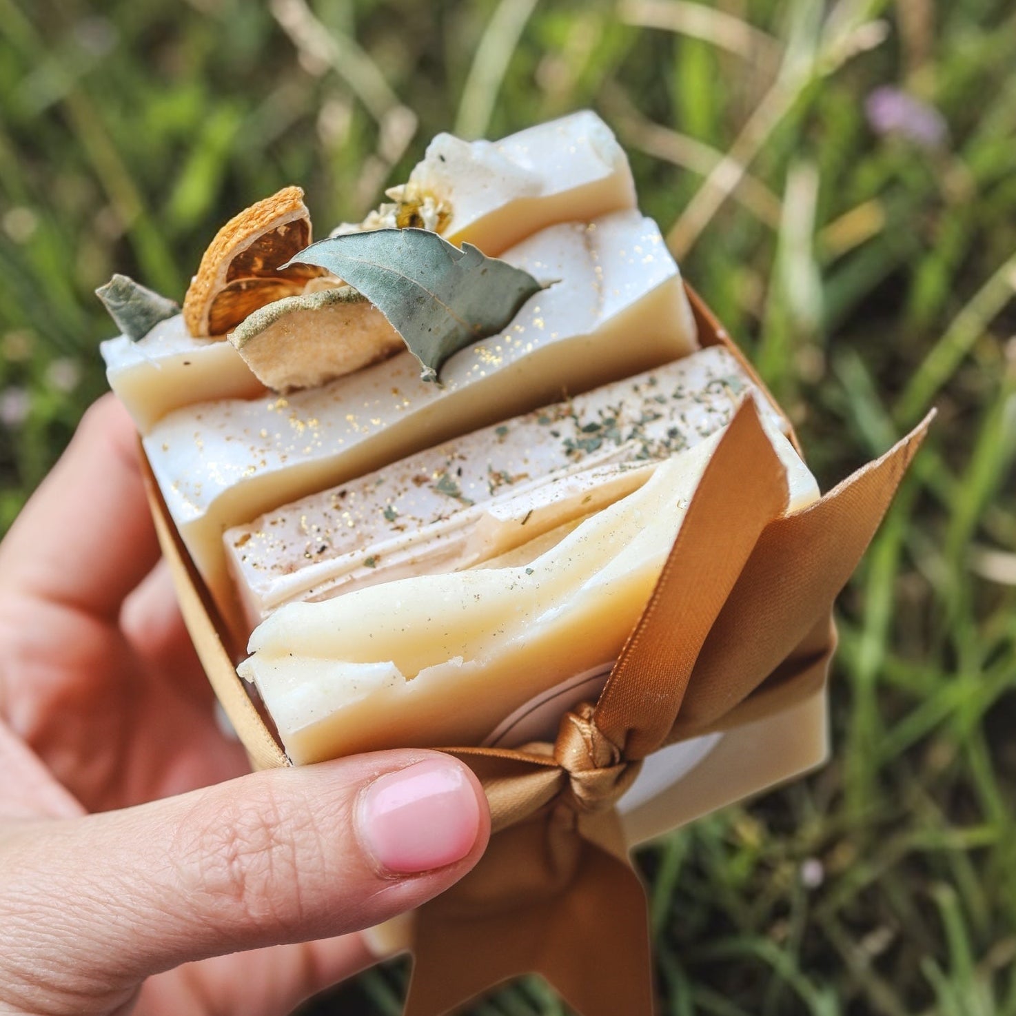 Hand holding a small bundle of soap bars against a grassy background